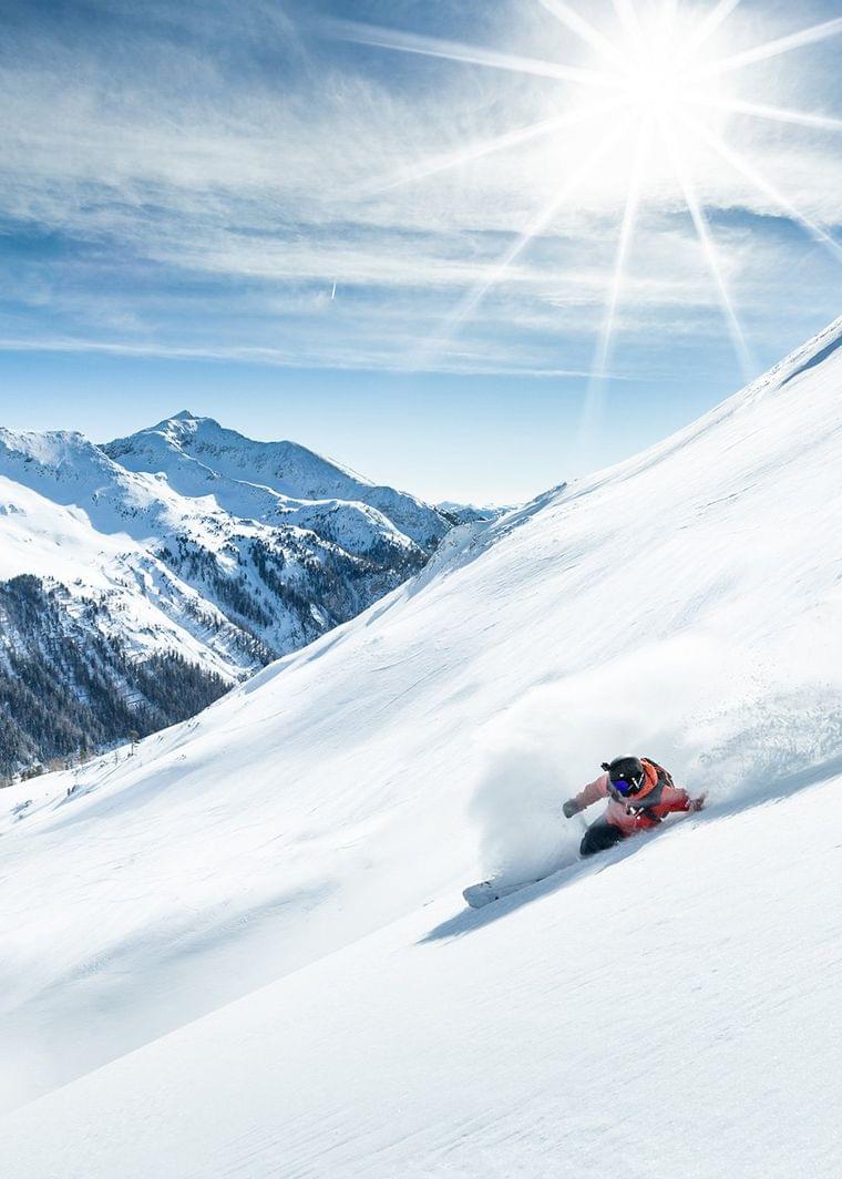 Skifahrer fährt durch frischen Pulverschnee am sonnigen Berghang